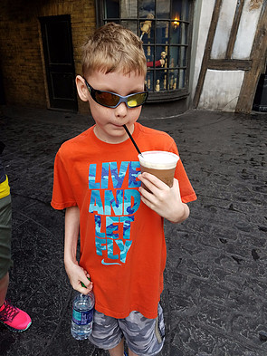 little boy drinking glass of butterbeer through straw