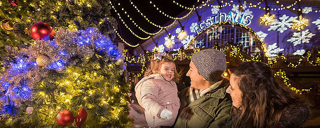 parents and toddler in front of outdoor decorated Christmas tree