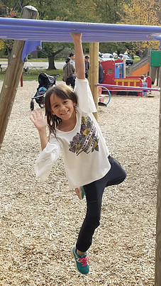 young girl smiling and waving on playground equipment